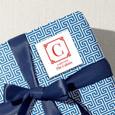 A gift wrapped in blue and white patterned paper with a blue ribbon tied around it, featuring a white label with a red letter "C" and text that reads "a gift from The Cabots".