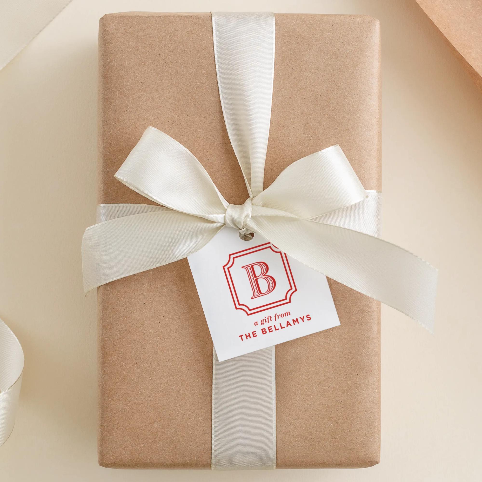 A brown gift box with a white ribbon and a white tag with a red "B" logo, placed on a beige surface.