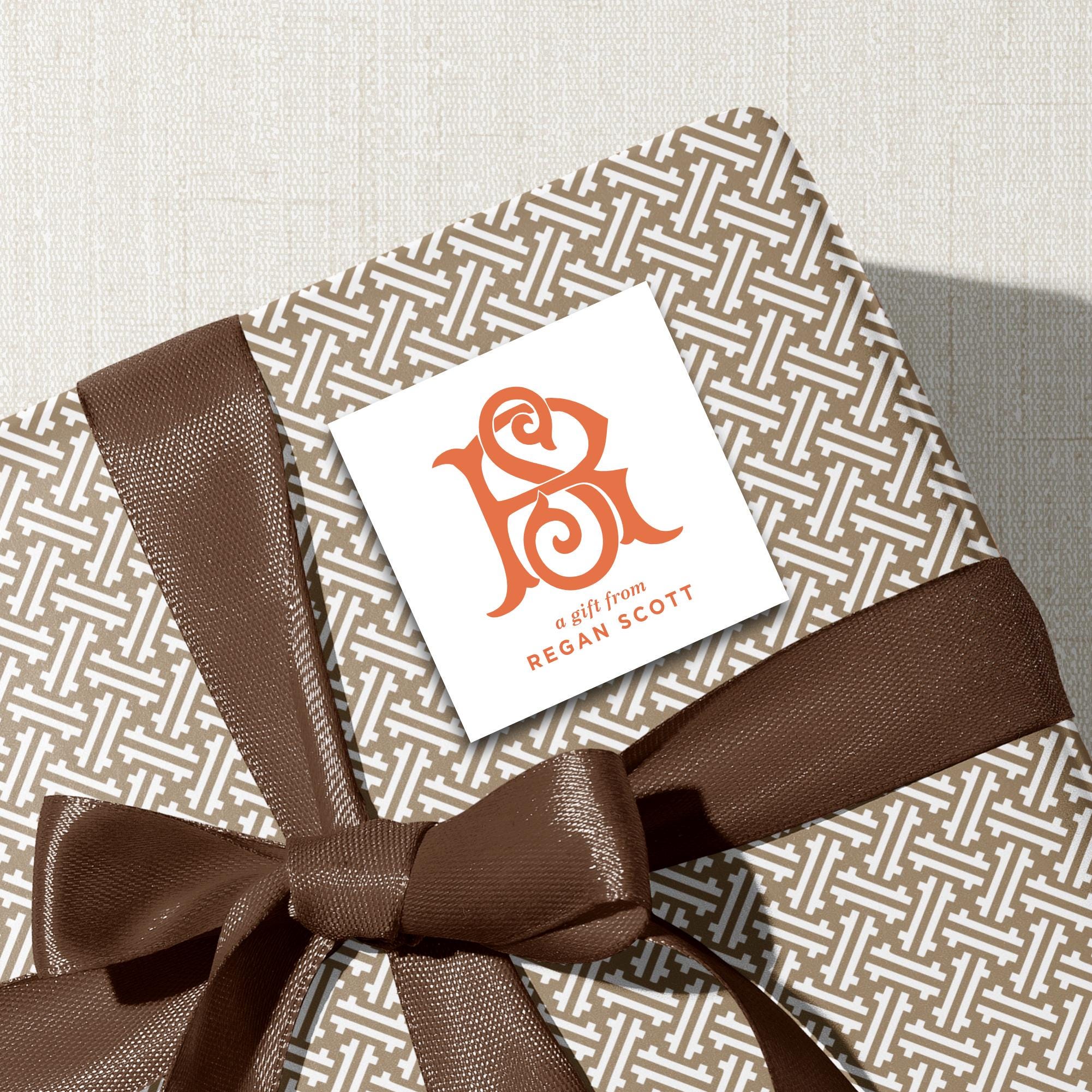 A gift wrapped in brown paper with a brown ribbon tied around it, featuring a white label with an orange logo and text.