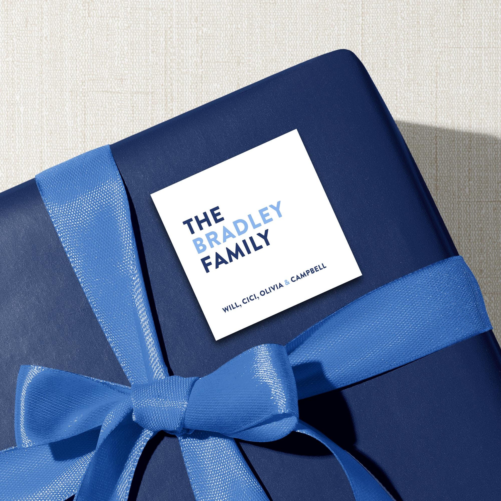 A blue gift box with a blue ribbon tied around it, featuring a white label with the text "THE BRADLEY FAMILY WILL CECIL OLIVIA & CAMBRELL" printed on it.