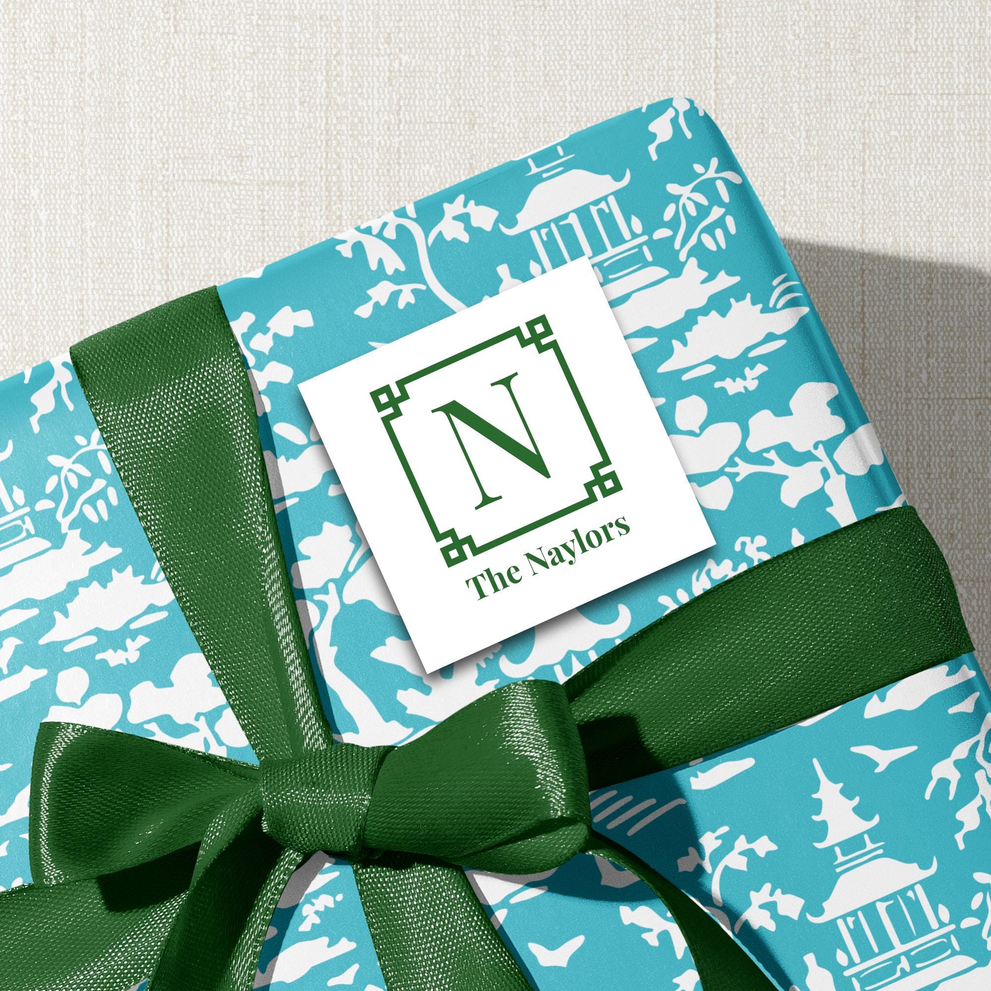 A gift wrapped in a blue and white patterned paper with a green ribbon, featuring a white label with the text "The Nayslors" and a green ribbon bow.