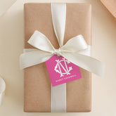 A gift box wrapped in brown paper with a white ribbon and a pink tag featuring a monogram logo.