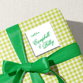 A gift wrapped in a green and white checkered paper with a green ribbon tied around it, featuring a white label with the text "a gift from Campbell & Billy".