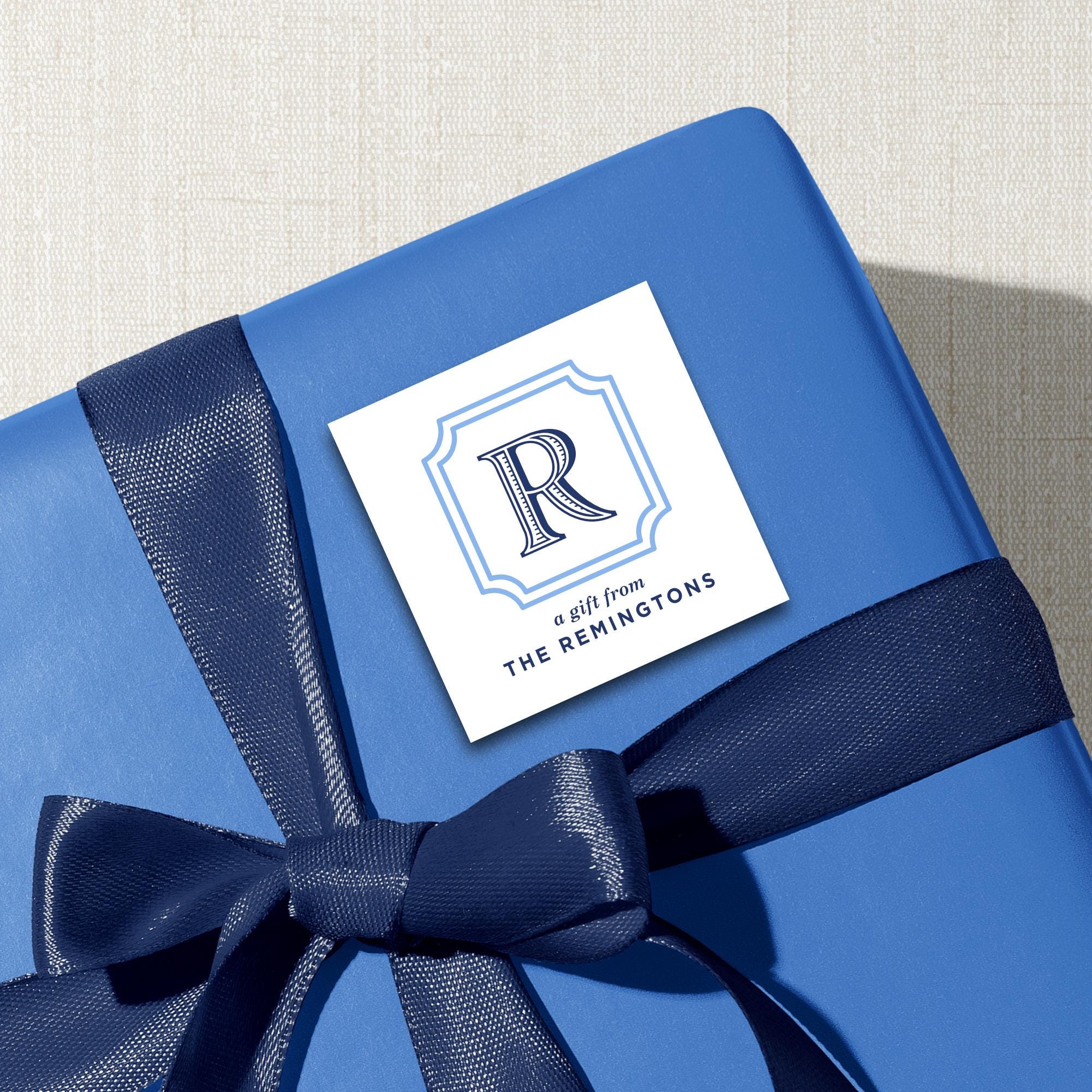 A blue gift box with a blue ribbon tied around it, and a white label with a blue ribbon and the text "A gift from THE REMINGTONS" printed on it.