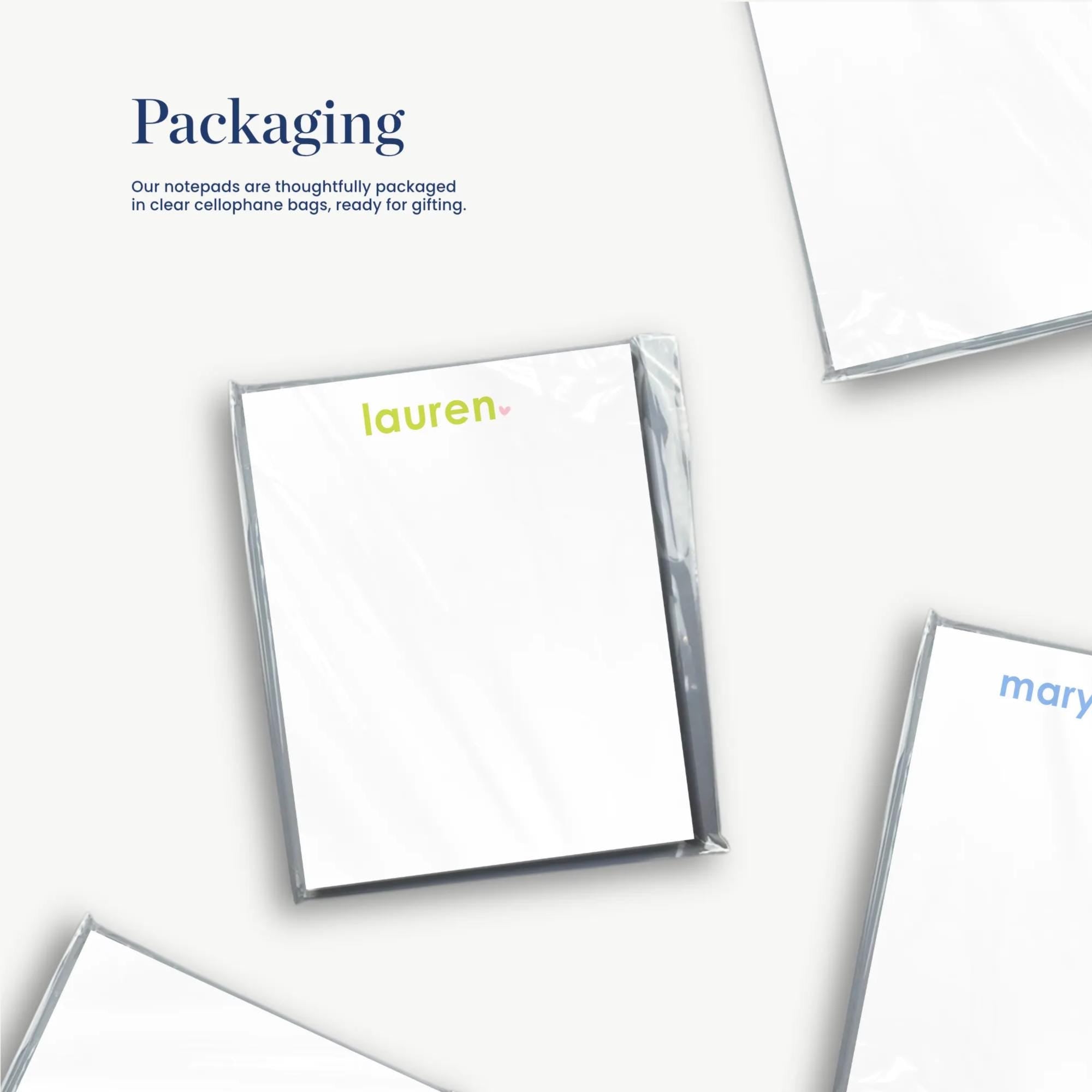 several white pieces of paper or cardstock, some of which are folded or cut, and there is a text overlay that reads "Packaging" and "Our notebooks are thoughtfully packaged in clear cellulosephore bags ready to gifting."