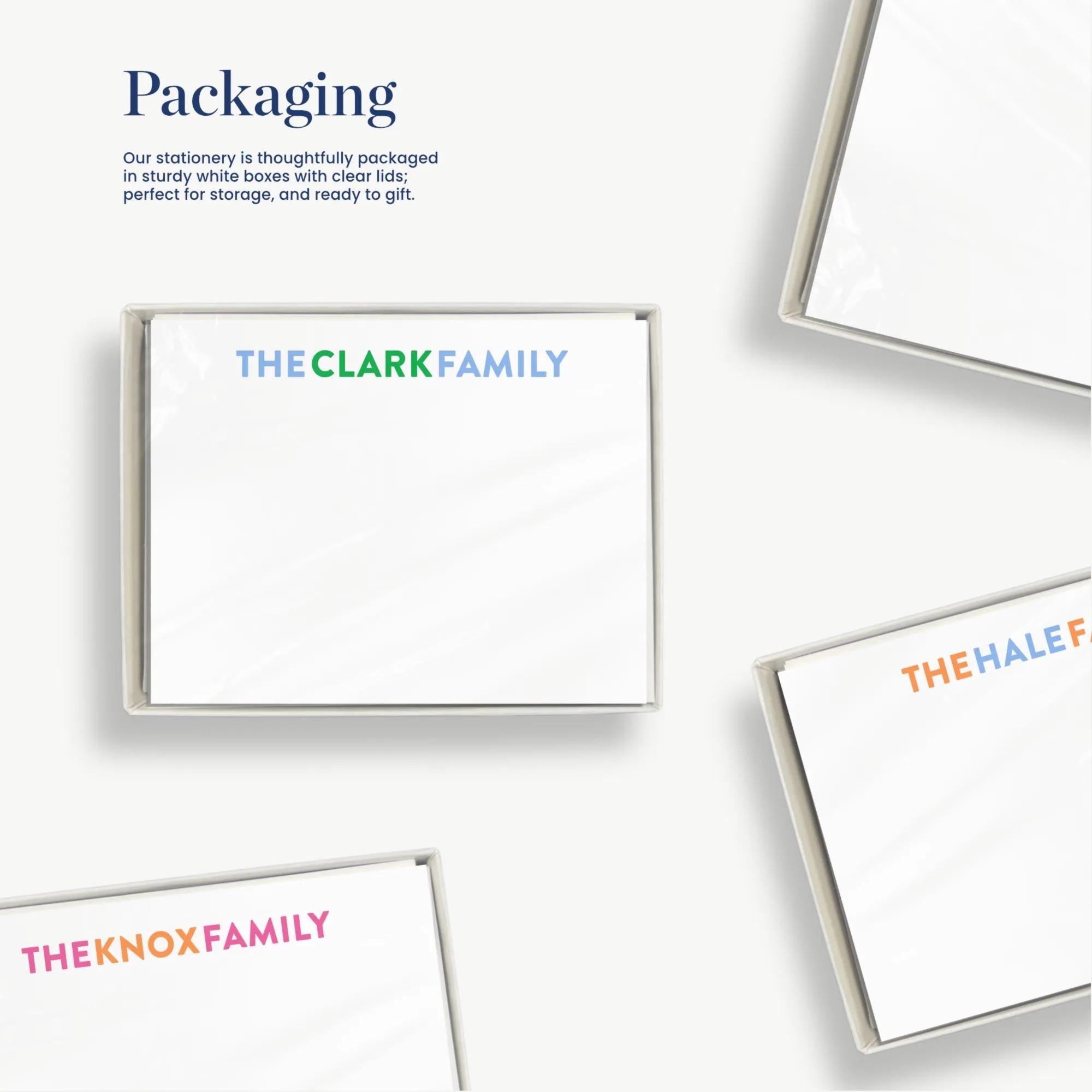 several white boxes with text on them, including "THE CLARK FAMILY", "THE HALF FAMILY", and "THE KNOX FAMILY". The boxes appear to be part of a packaging design, and the text suggests that the stationery is thoughtfully packaged in sturdy white boxes with clear lids for easy storage and ready-to-give.