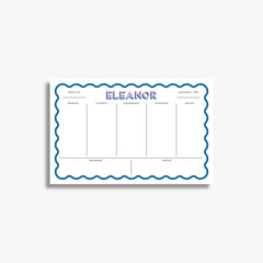A white schedule planner with the name "ELEANOR" written in large blue letters. The planner has a scalloped edge and is divided into sections for each day of the week, with blank spaces for notes.